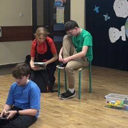 Aktorzy szkolnego teatrzyku podczas przedstawienia - starsza uczennica pakuje młodszemu koledze książki.