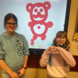 Uczennice na tle tablicy z własnoręcznie narysowanym misiem.