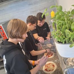 Uczniowie przygotowujący pizzę przy pomocy szefa kuchni 