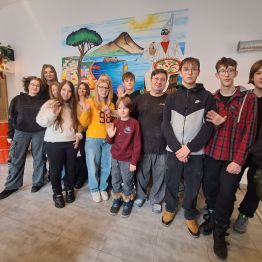 Grupa uczniów wraz z szefem kuchni na tle grafiki przedstawiającej Neapol