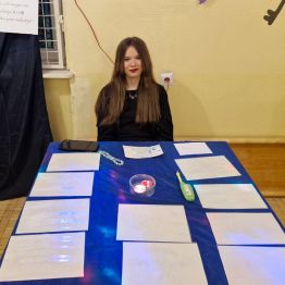 Wróżka siedzi przy stanowisku z wróżbą: „mowa kwiatów”.