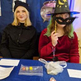 Wróżbici siedzą przy stanowisku z wróżbą: „rzut kośćmi” oraz „moneta w studni”.