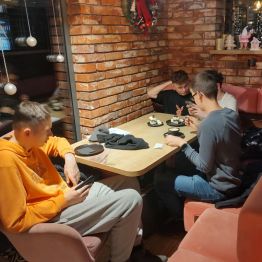 Wychowankowie spędzają czas w przytulnej kawiarni, siedząc przy stolikach z kawą i deserami w zimowo-świątecznej atmosferze.