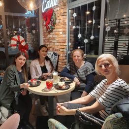 Wychowawcy siedzą przy stoliku z kawą i deserami w zimowo-świątecznej atmosferze.