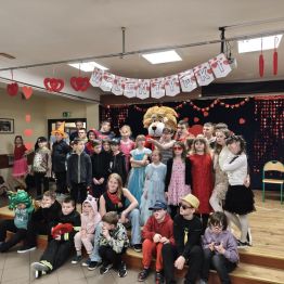 Młodsi uczniowie stoją na scenie razem z maskotką ZPSW lwem Leonem