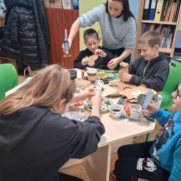 Grupa uczniów przygotowuje kawowe serca pod nadzorem wychowawczyni.