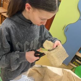 Uczennica wycina szablon serca z juty.