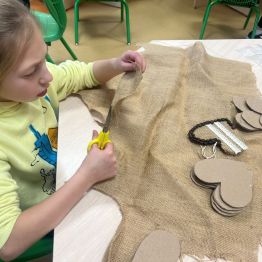 Uczennica wycina szablon serca z juty.