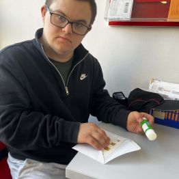 Dawidek siedzi i przykleja znaczek do koperty.