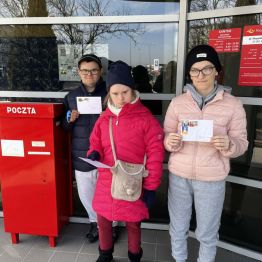 Kasia, Malwinka i Dawid stoją przy skrzynce pocztowej. W rękach trzymają zaadresowane do swoich domów koperty z widokówkami w środku.