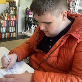 Kamil siedzi i pisze życzenia.