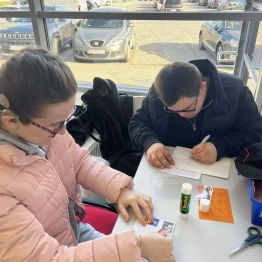 Dawid pisze życzenia. Malwinka przykleja znaczki.