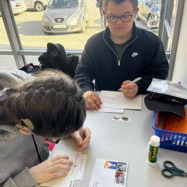 Malwinka i Dawid siedzą przy stole i wypisują życzenia.