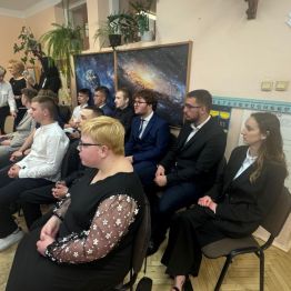 Absolwenci siedzą na krzesłach w czasie uroczystości.