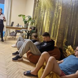 Wychowawca wprowadza wstęp do tematu zajęć o smutku, a wychowankowie leżą w kręgu na pufach.