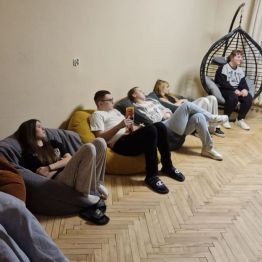 Wychowawca wprowadza wstęp do tematu zajęć o smutku, a wychowankowie leżą w kręgu na pufach.