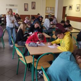 Uczniowie siedzą przy stoliku i piszą pracę konkursową