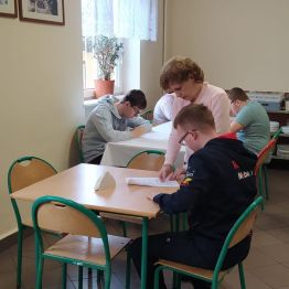 Uczniowie siedzą przy stoliku i piszą pracę konkursową
