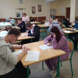 Uczniowie siedzą przy stoliku i piszą pracę konkursową
