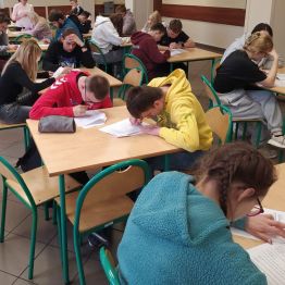Uczniowie siedzą przy stoliku i piszą pracę konkursową