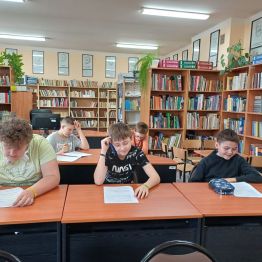 Uczniowie siedzą przy stoliku i piszą pracę konkursową