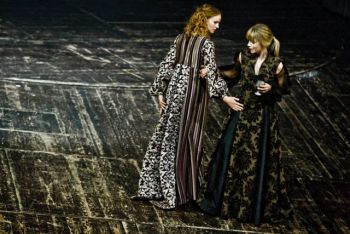 Aktorki w ciemnych, długich sukniach na teatralnej scenie.