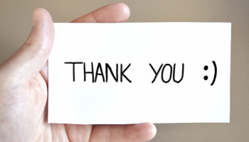 Dłoń trzymająca białą karteczkę z czarnym napisem: THANK YOU :)