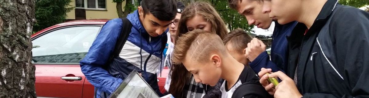 Uczniowie na spacerze w mieście patrzą na tablicę informacyjną.