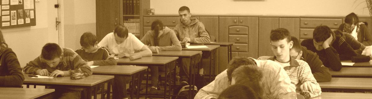 Uczniowie siedzą w ławkach i pochylają się nad sprawdzianami
