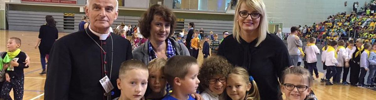 Nauczycielki, ksiądz i uczniowie uśmiechają się