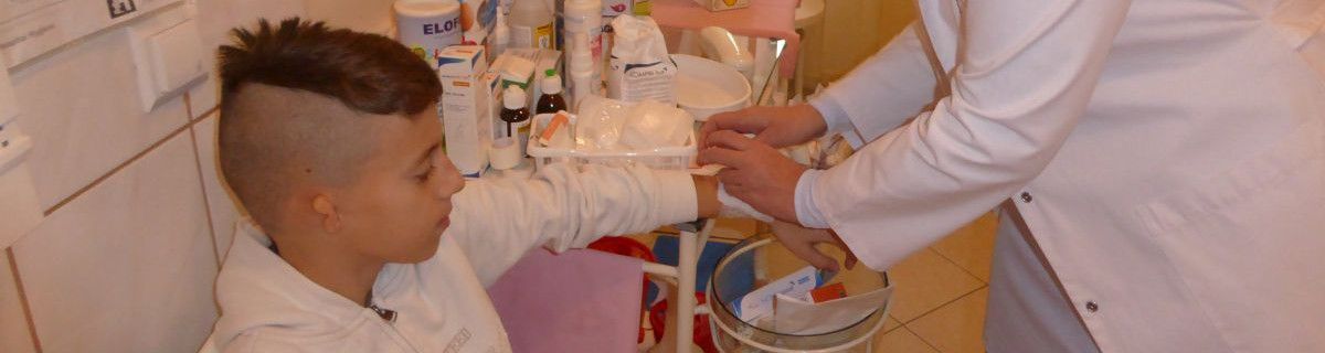 Szkolna pielęgniarka zakłada uczniowi opatrunek na ręce