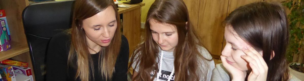 Pani psycholog i dwie uczennice siedzą obok siebie i spoglądają w dół.