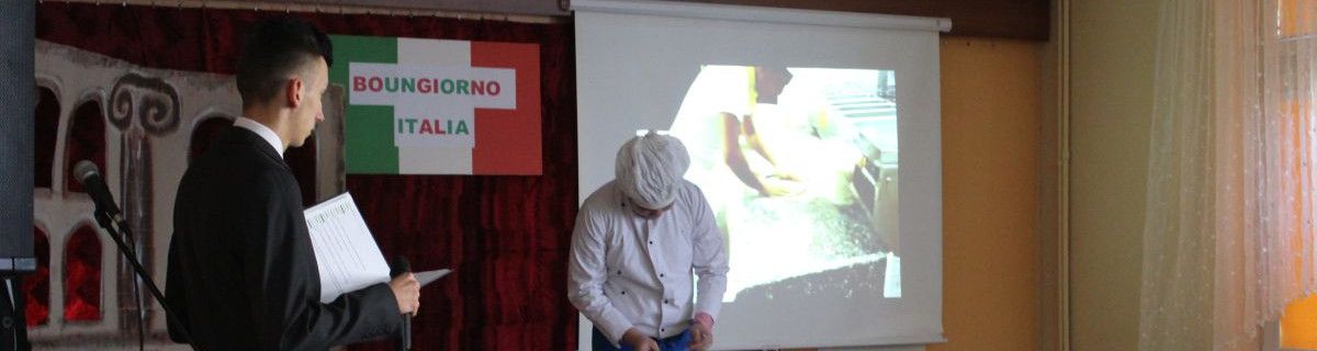 Na scenie stoi dwoje uczniów, jeden w stroju kucharza schyla głowę, drugi w garniturze trzyma kartki z tekstem