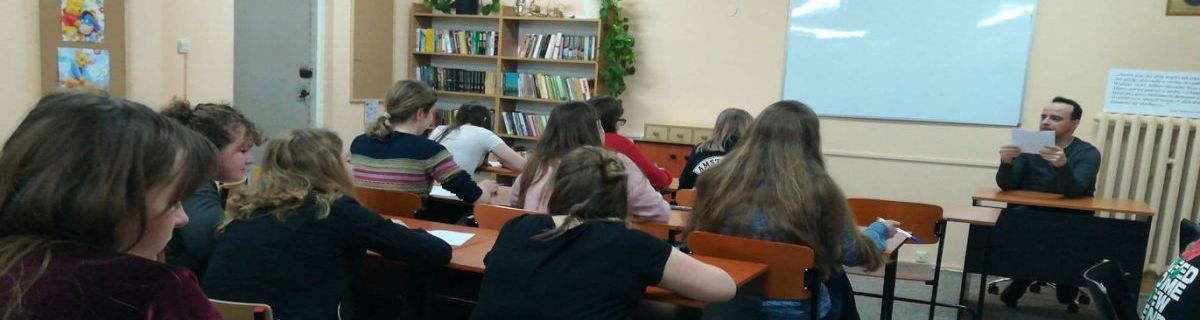 Grupa uczniów siedzących w ławkach, z przodu nauczyciel prowadzący zajęcia