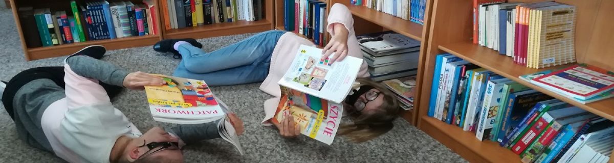 Dwie dziewczynki leżą na podłodze w szkolnej bibliotece i czytają ksiązki