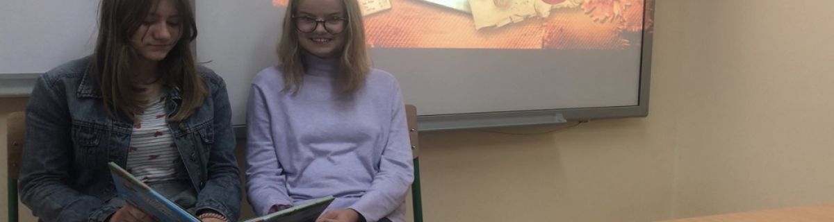 Dwie uczennice siedzą obok siebie i trzymają otwartą, dużą książkę
