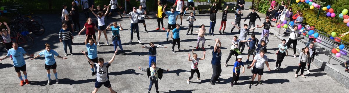 Duża grupa uczniów tańczy przed szkołą
