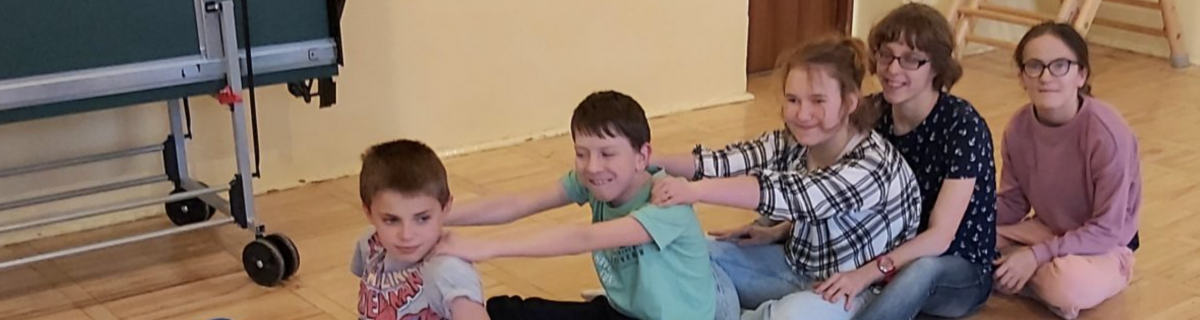 Uczniowie siedzą w rządku na podłodze w sali gimnastycznej