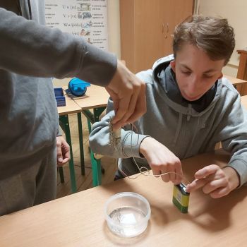 Wychowankowie przeprowadzają doświadczenie z elektromagnes. Jeden uczeń trzyma elektromagnes do którego są przyczepione szpilki(dużą ilość). Drugi łączy przewody elektromagnesu z baterią. Przepływ prądu przez elektromagnes powoduje że wytwarza się pole magnetyczne i elektromagnes przyciąga żelazo czyli szpilki,