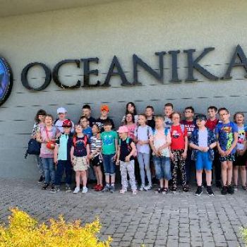 Grupa uczniów z klas I-IV pozuje do zdjęcia przed budynkiem Oceaniki.