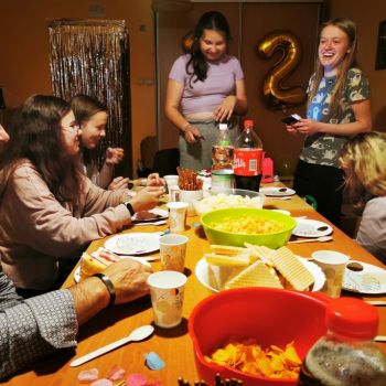 Dzieci i młodzież przy stole zastawionym słodyczami i ciastami. 