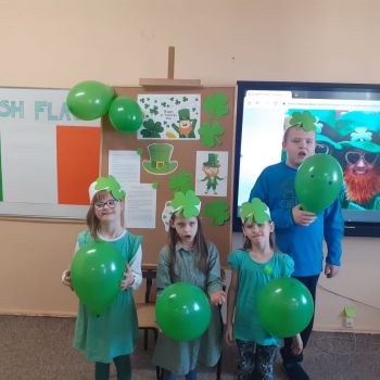 Grupka uczniów w zielonych ubraniach trzyma w rękach zielone balony. W tle flaga Irlandii.