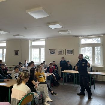 Grupa uczniów w szkolnej stołówce słucha przemawiającego policjanta