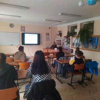 rodzice siedzą w ławkach, w tle tablica interaktywna, biurko i nauczyciel