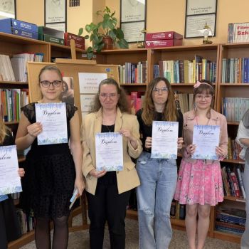 Laureaci konkursu trzymają w rękach dyplomy. W tle regały z książkami.