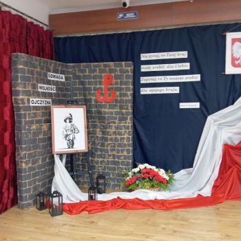 Wystrój podczas akademii: flaga, godło, kwiaty, napisy, portret Powstańca