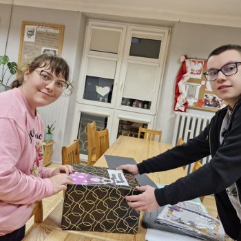 Wychowankowie przyklejają elementy na pudełko Andrzejkowe 