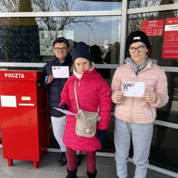 Kasia, Malwinka i Dawid stoją przy skrzynce pocztowej. W rękach trzymają zaadresowane do swoich domów koperty z widokówkami w środku.