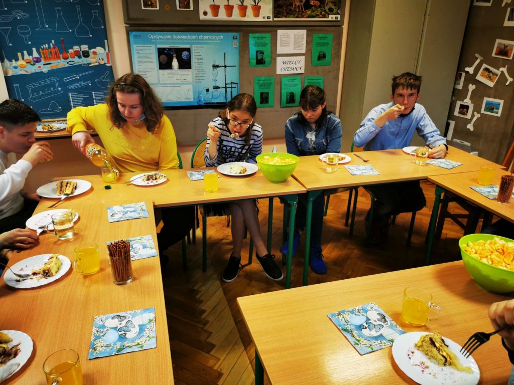 Uczniowie siedzą w ławkach i jedzą tort