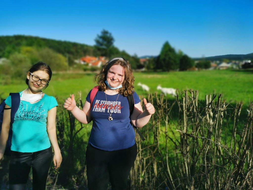 Dwie uczennice uśmiechają się, za nimi pole i kozy